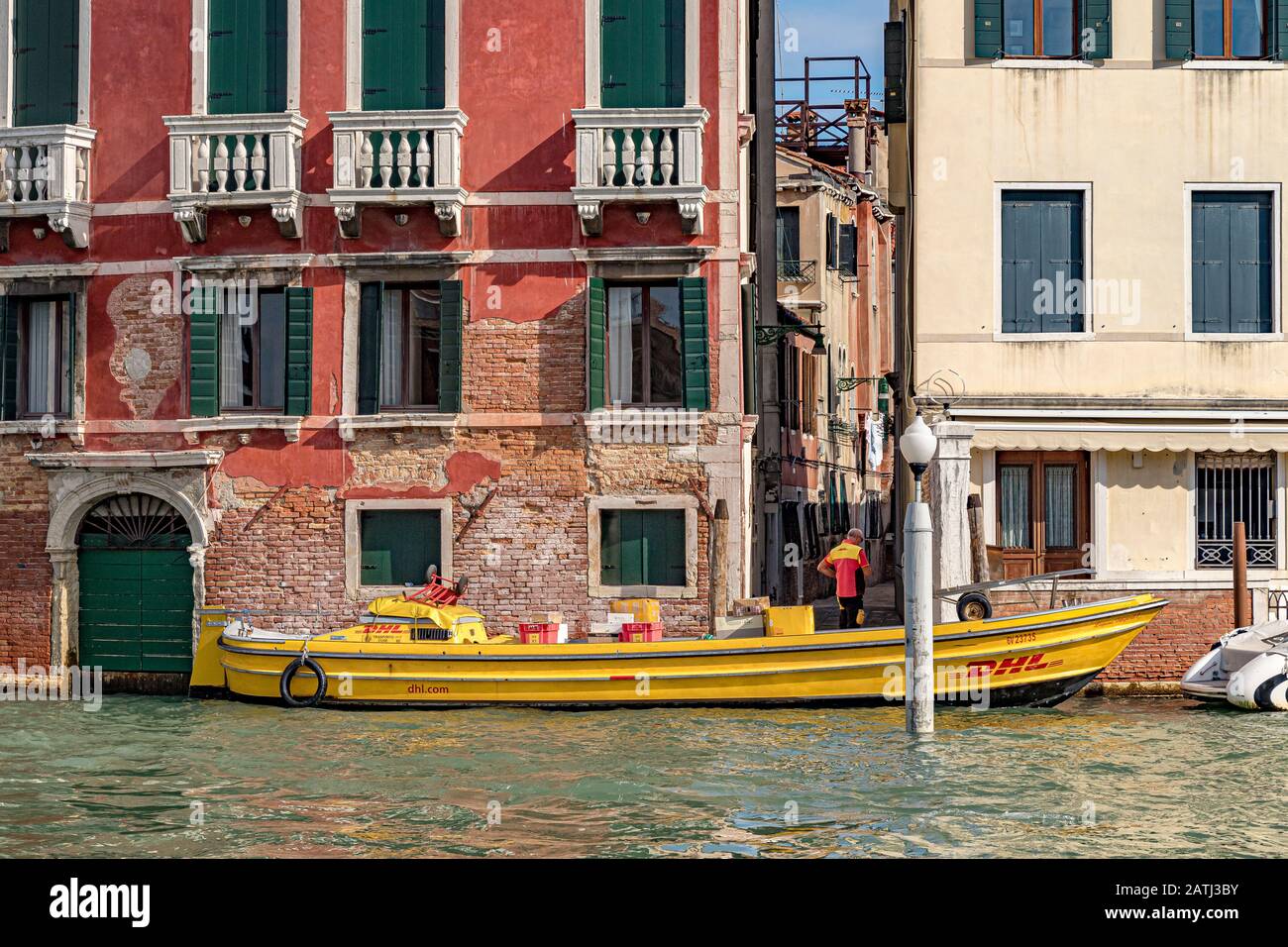 A DHL delivery driver leaves his DHL courier delivery boat , filled with parcels and packages makes his deliveries around the canals of Venice ,Italy Stock Photo