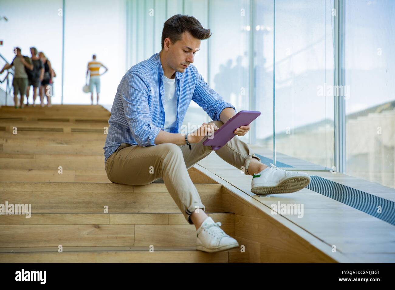 Man using tablet, sitting on steps at big windows, big working space. Stock Photo