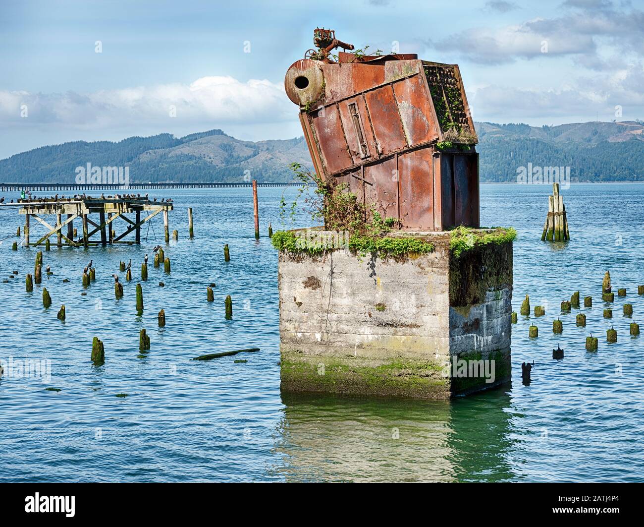 A piece of iron equipment on a huge concrete pillar stands amid the ruins of an old pier on the Columbia River in Astoria. Stock Photo
