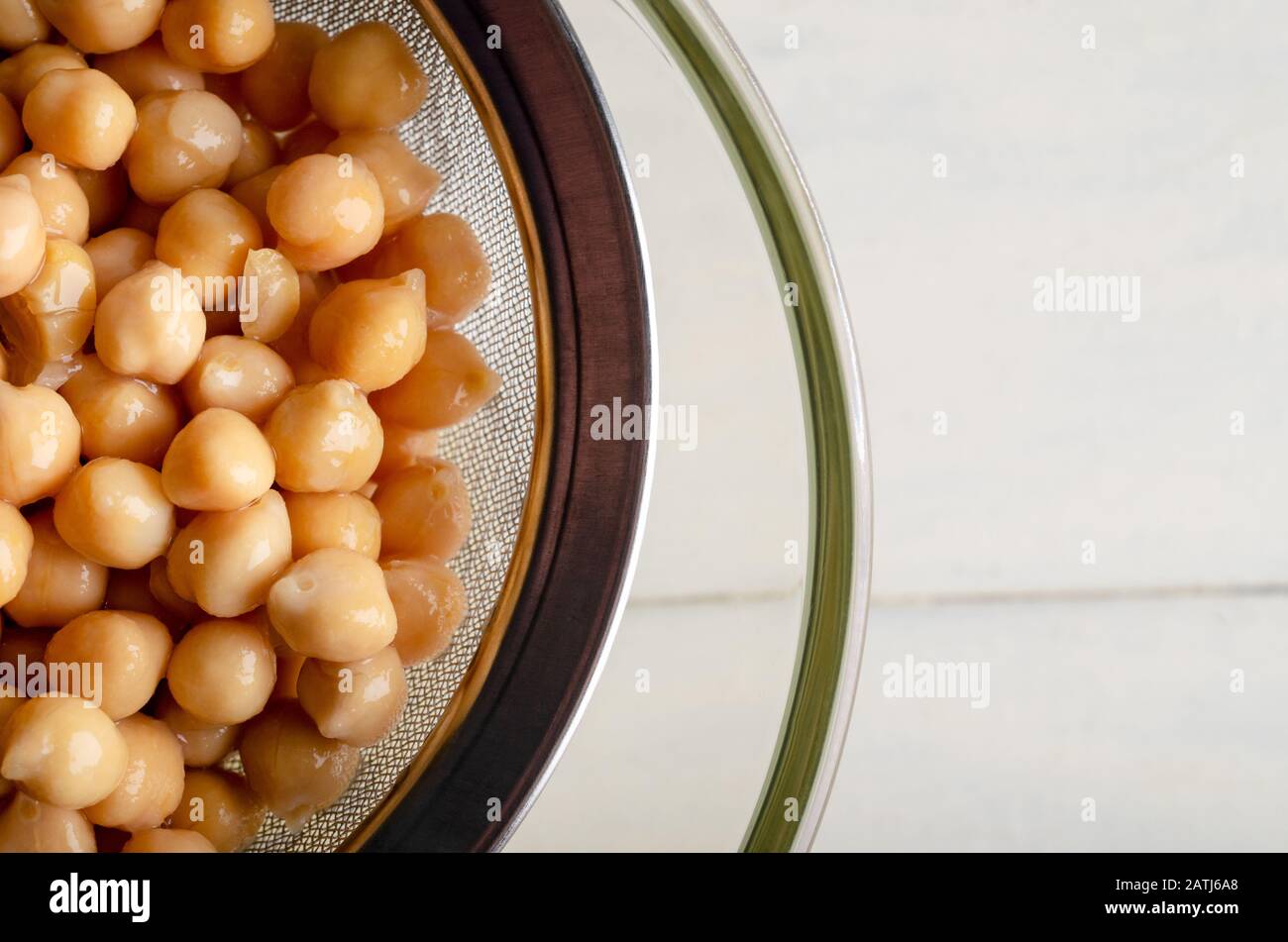 Overhead shot of chickpeas being strained through a metal sieve into a glass bowl to release aquafaba. Copy space to right. Stock Photo