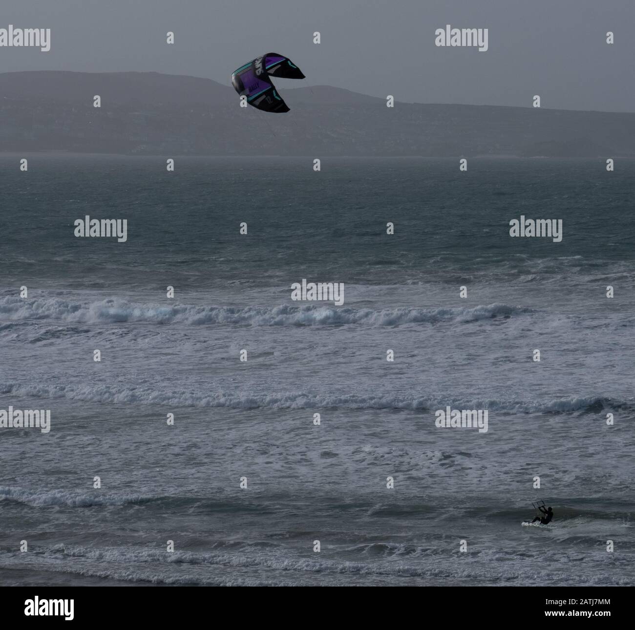 Tiny looking kite surfer on the waves of Gwithiwn beneath a curved kite