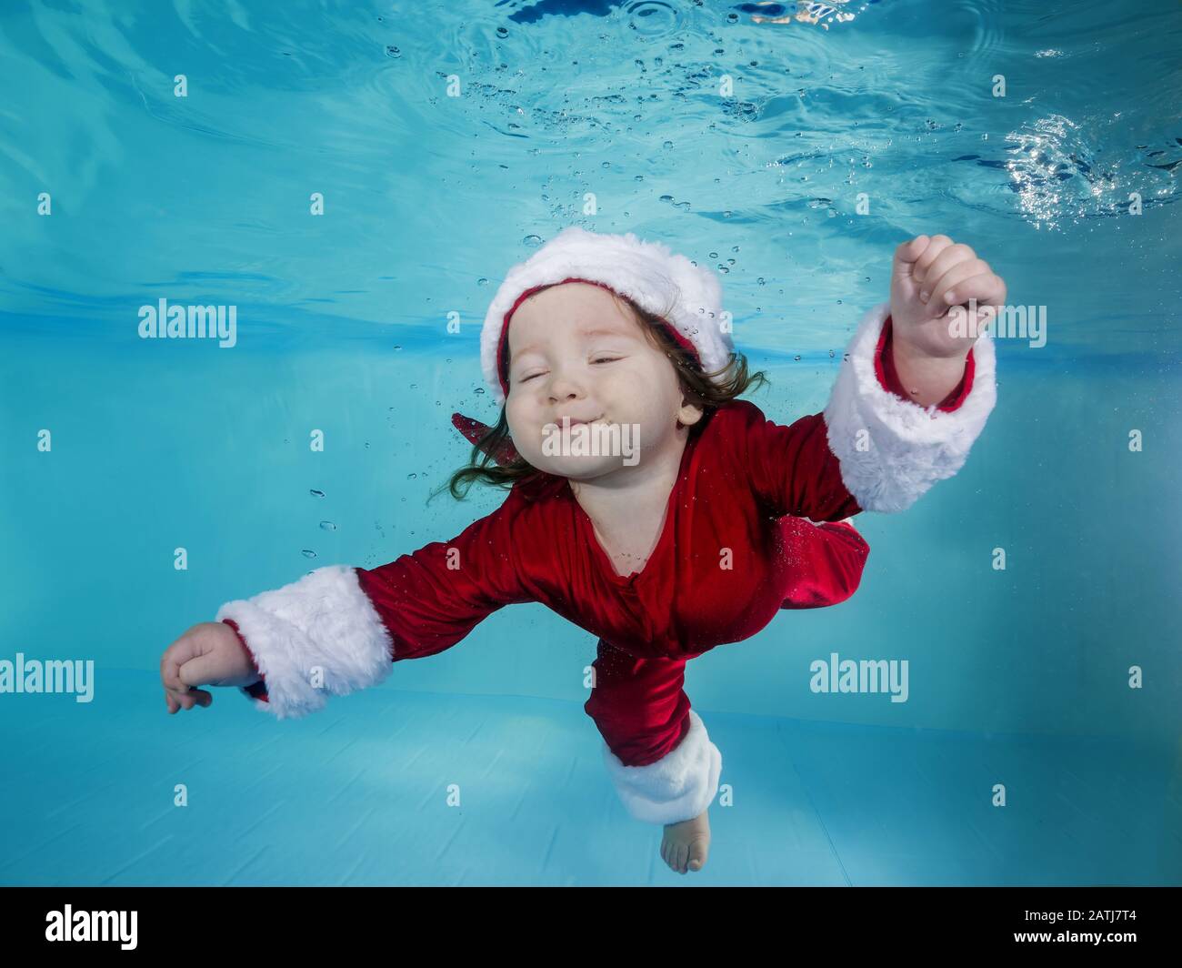 Funny longhaired boy in a Christmas outfit dives underwater in a