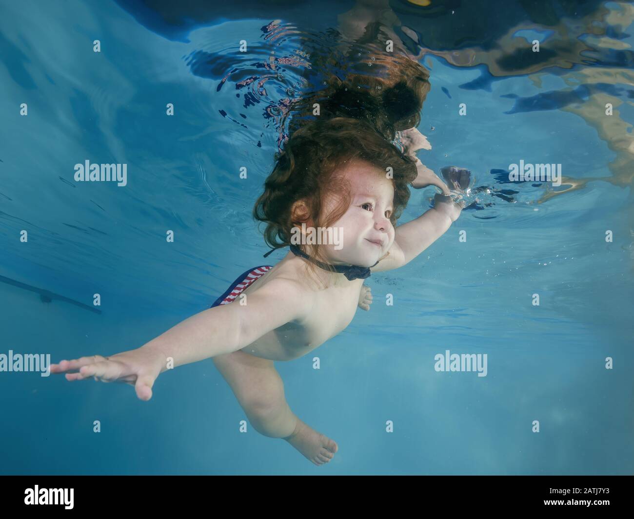 Funny longhaired boy dives underwater in a swimming pool Stock Photo
