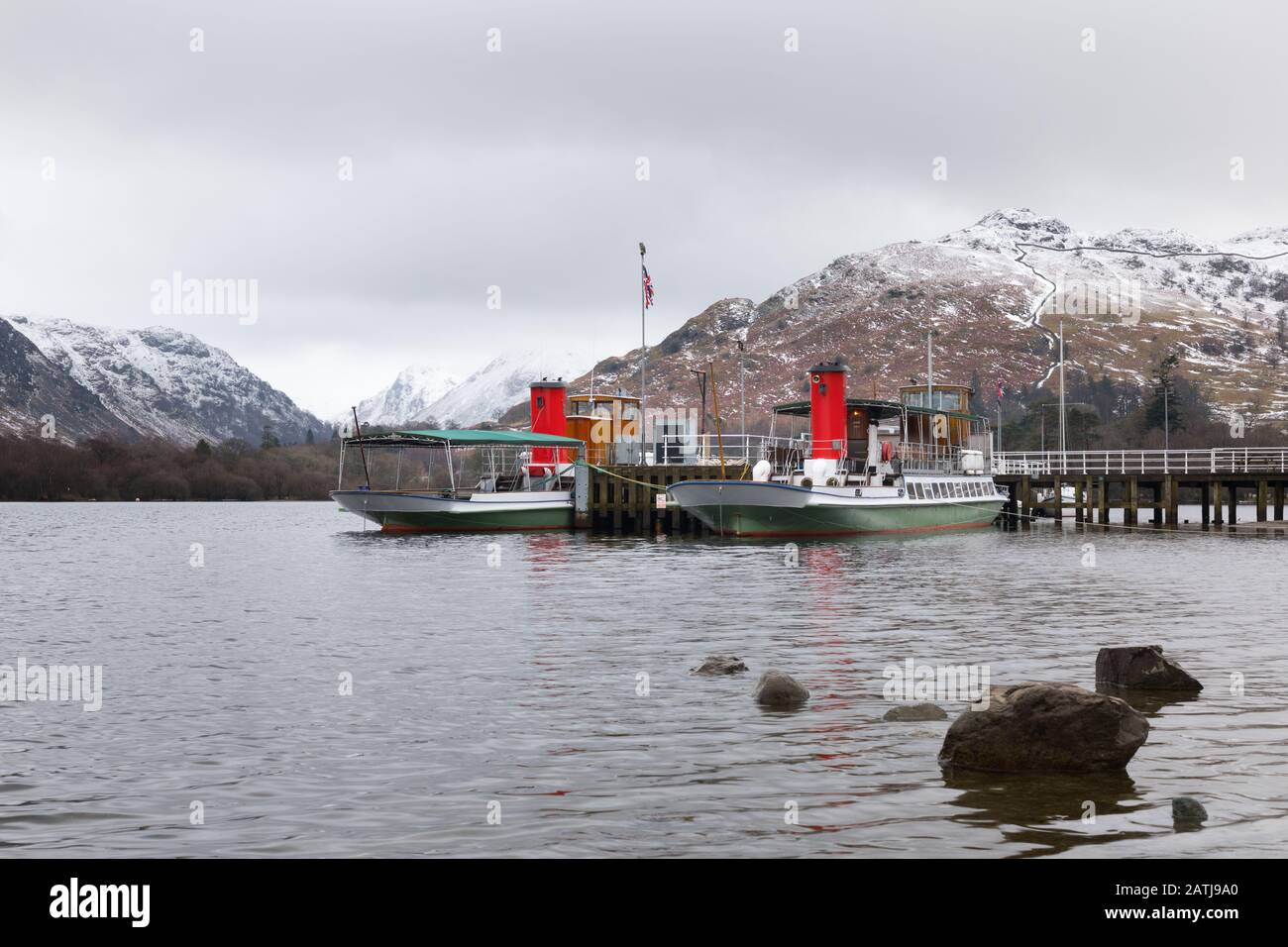 Glenridding, Cumbria, Lake District: Ullswater 'Steamers' boats Lady of the Lake and Raven moored at Glenridding pier with snow-covered fells behind. Stock Photo