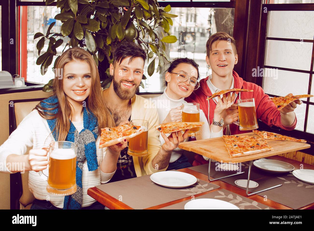 The company of young guys in a pizzeria with glasses of beer in their hands and large pieces of pizza. Friends party at the pub Stock Photo
