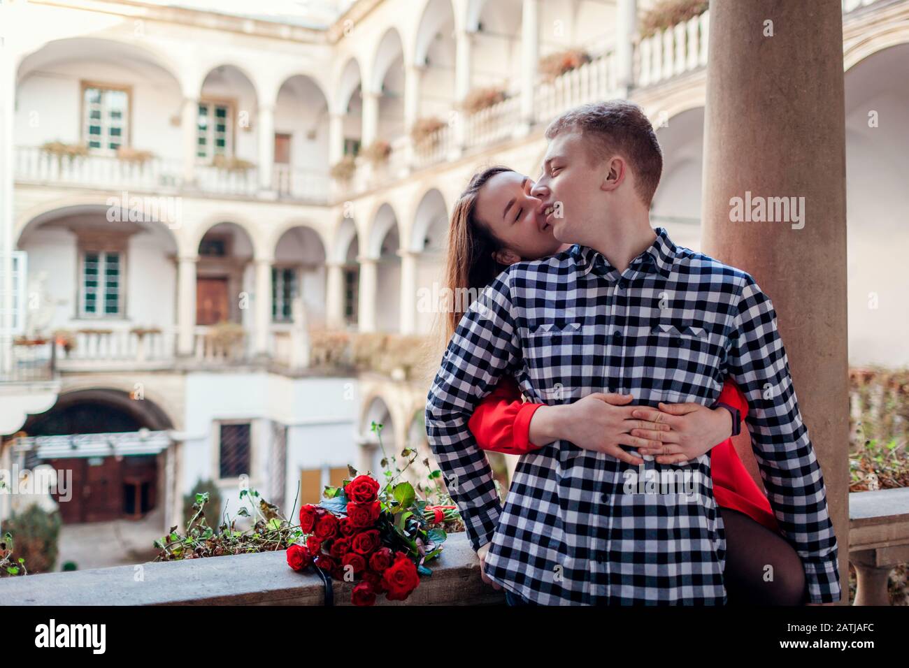 Valentines day romantic date. Woman kissing boyfriend on cheek. Couple hugging in italian yard in Lviv with roses Stock Photo