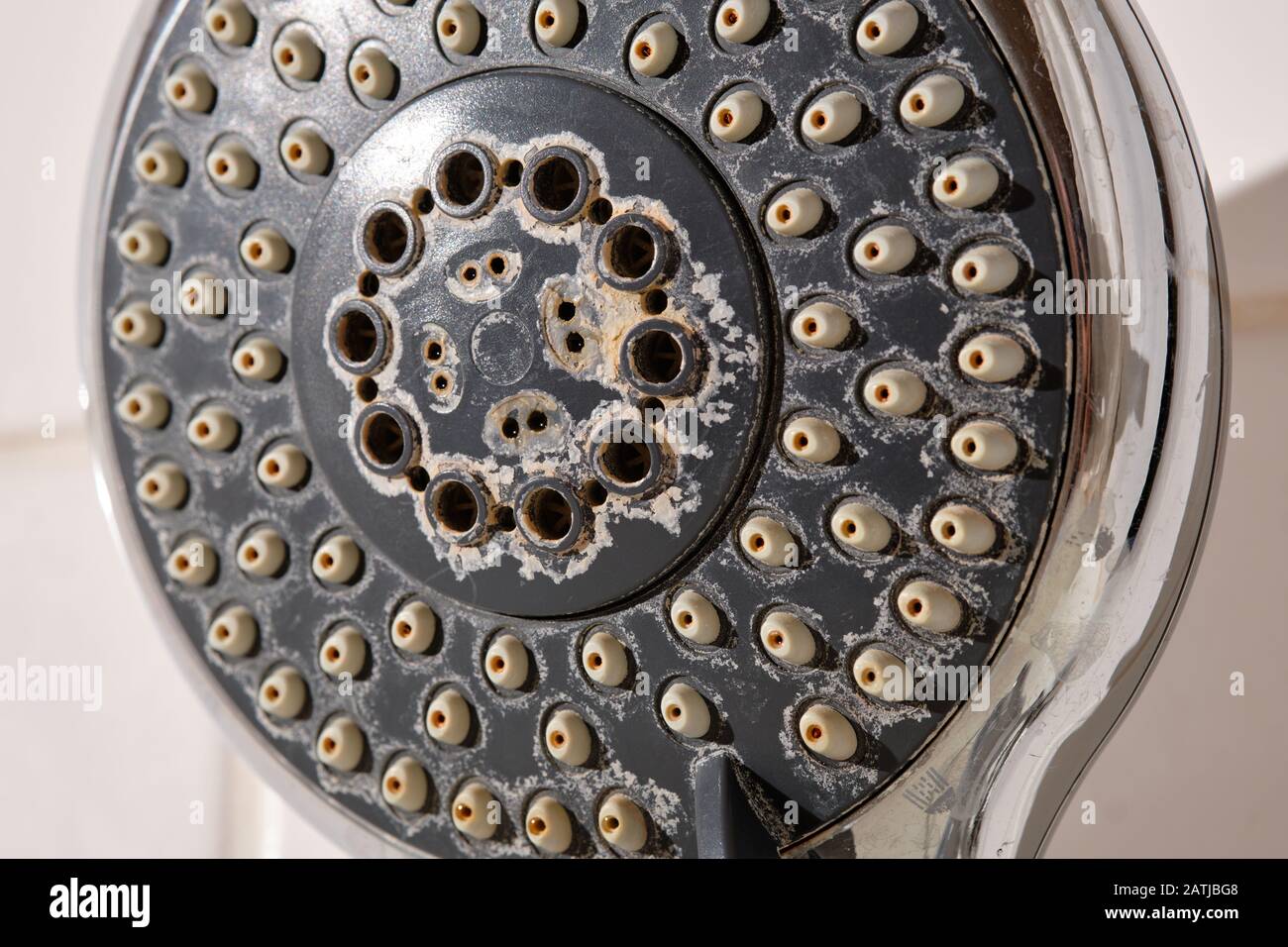 Close-up of an old used silver and grey colored shower head with limescales in the bathroom in front of white tiles Stock Photo