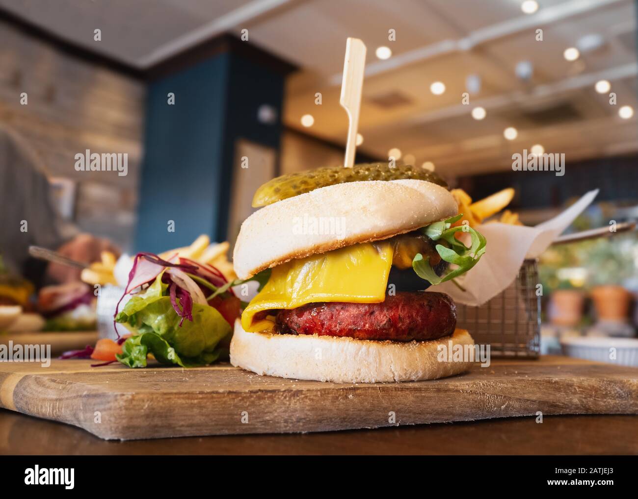 Melted cheese on a portobello mushroom and beetroot and bean vegetarian burger in a bun, on a wooden serving board, with a side salad and metal basket Stock Photo
