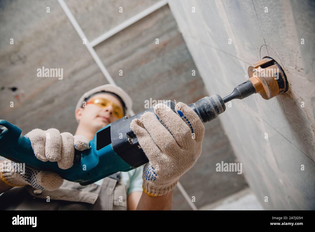 Builder worker pneumatic hammer drills hole in concrete brick wall with diamond crown for electric cable, socket, switch Stock Photo