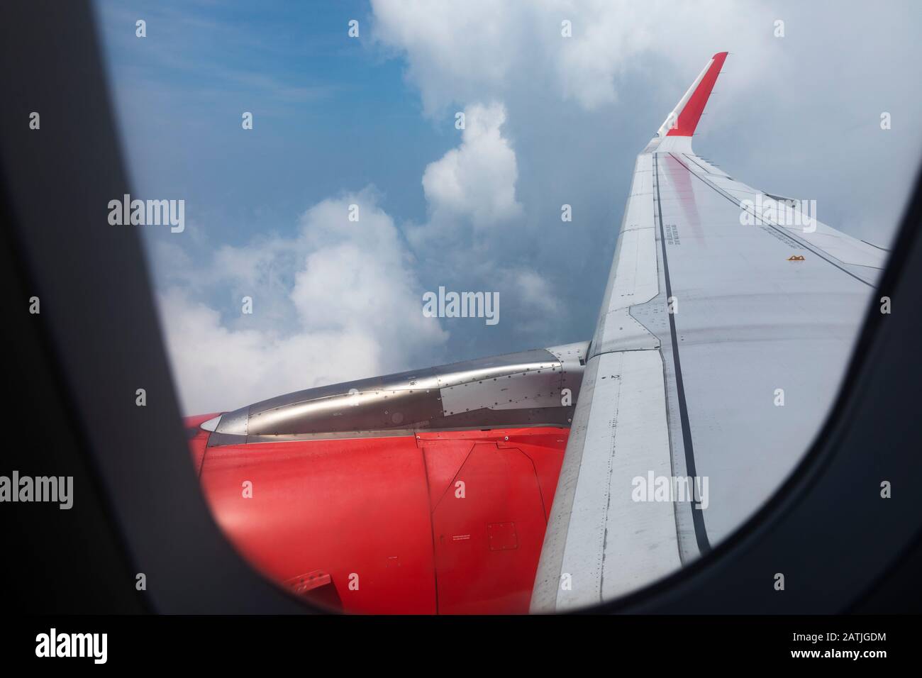 View from Airbus A320 Airplane window on a sunny day looking along the wing with red corporate badging, sunny sky and clouds Stock Photo