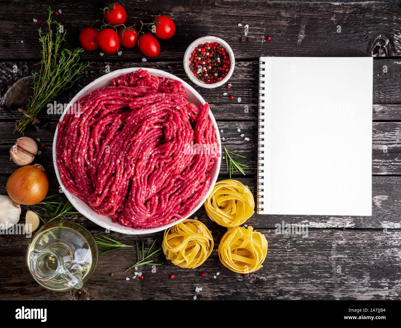 Mince beef, ground meat with ingredients for cooking on old gray dark wooden rustic table, notepad, recipe mock-up, top view, copy space. Stock Photo