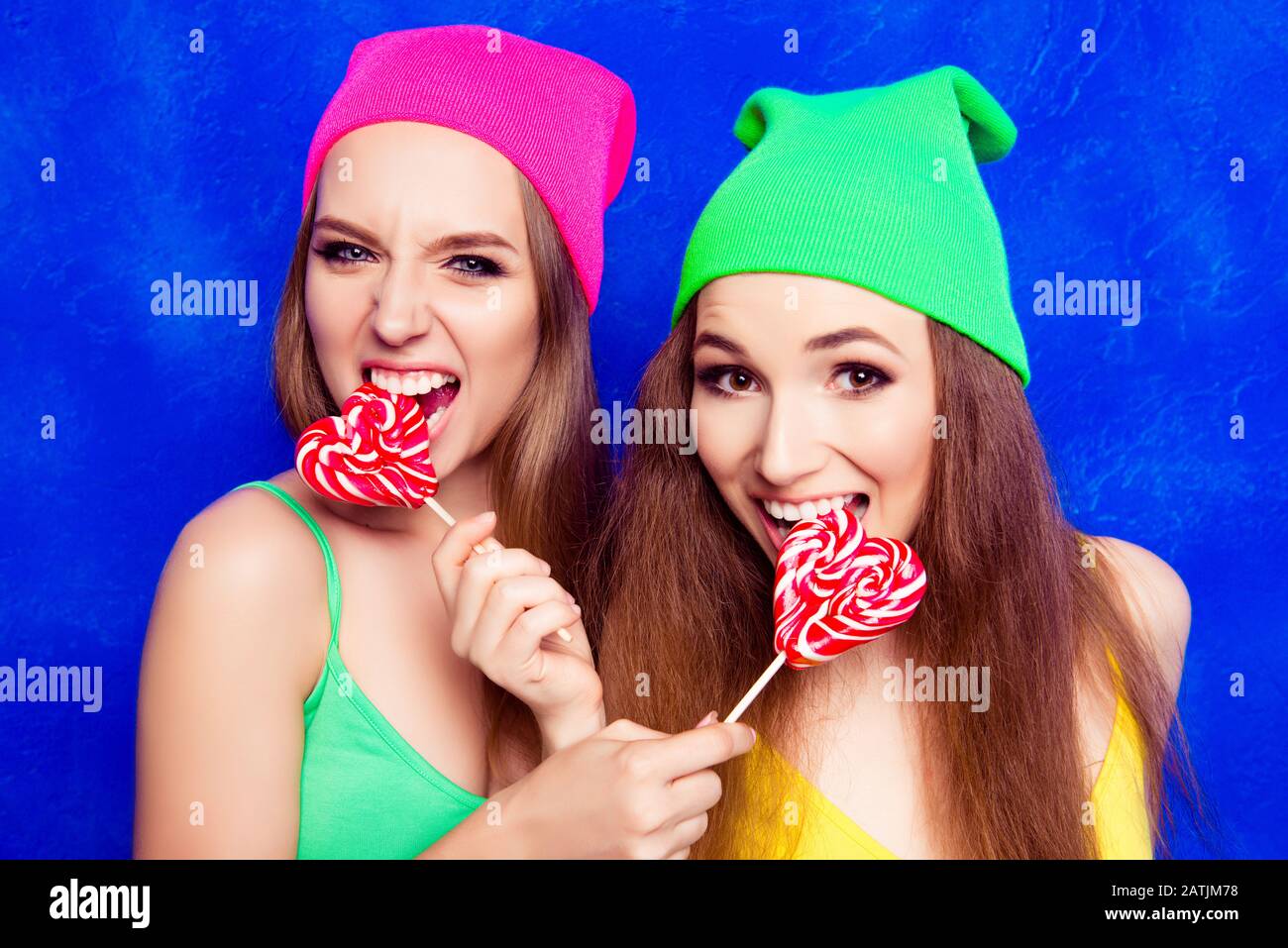 Portrait of attractive happy girls in hats biting lollipops Stock Photo