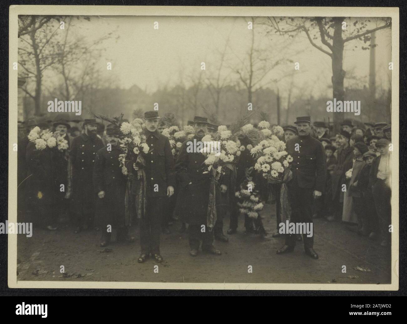 Description Funeral procession with large crowds; men in uniform carrying wreaths. Date {1914