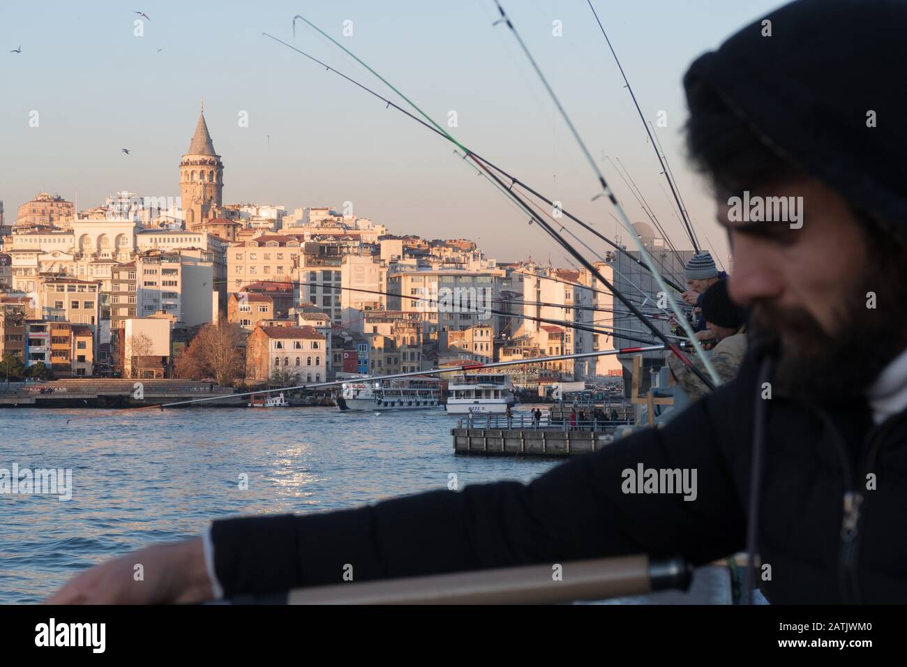 Istanbul, Turkey - Jan 10, 2020: Fishermen on the Galata Bridge, in Eminonu district , Galata Bridge is in background Beyoglu district, Istanbul. Turk Stock Photo