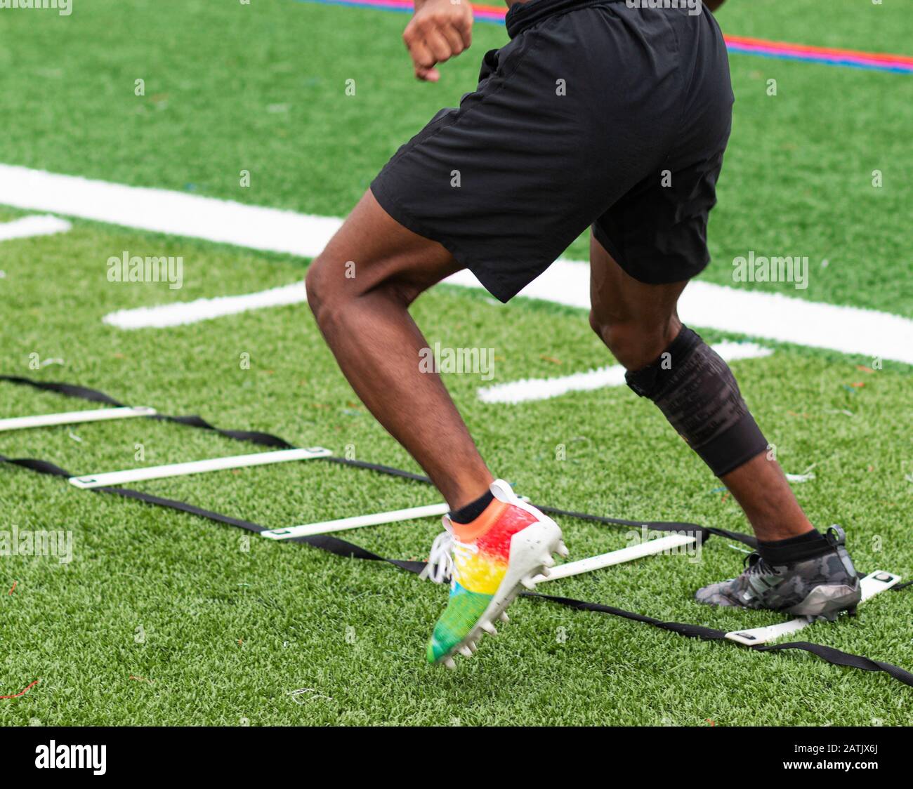 A high school boy is running ladder drills with colorful cleats on a turf field during summer camp practices. Stock Photo