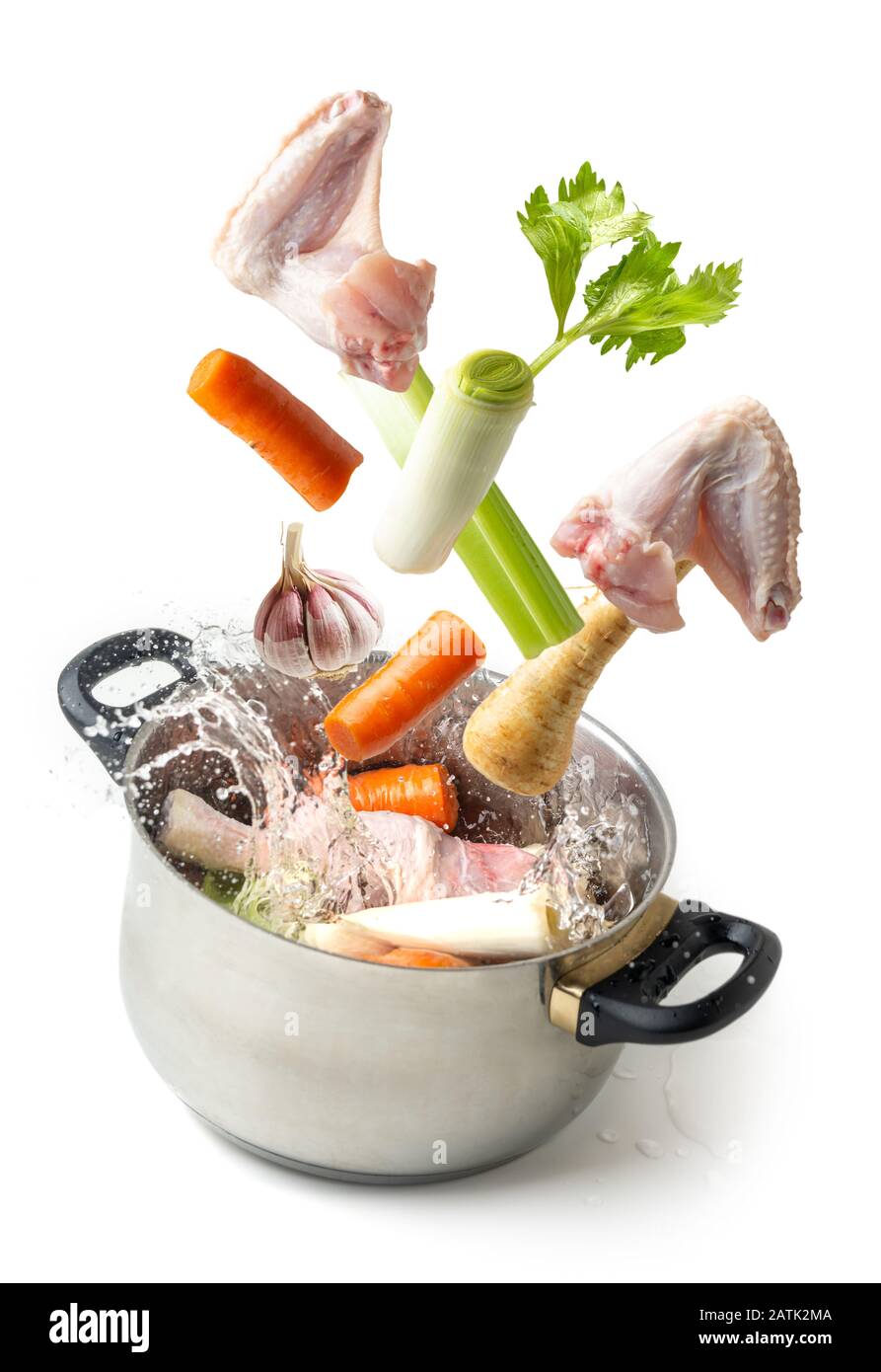 Ingredients for making broth flying towards a pot with splashing water on white background Stock Photo