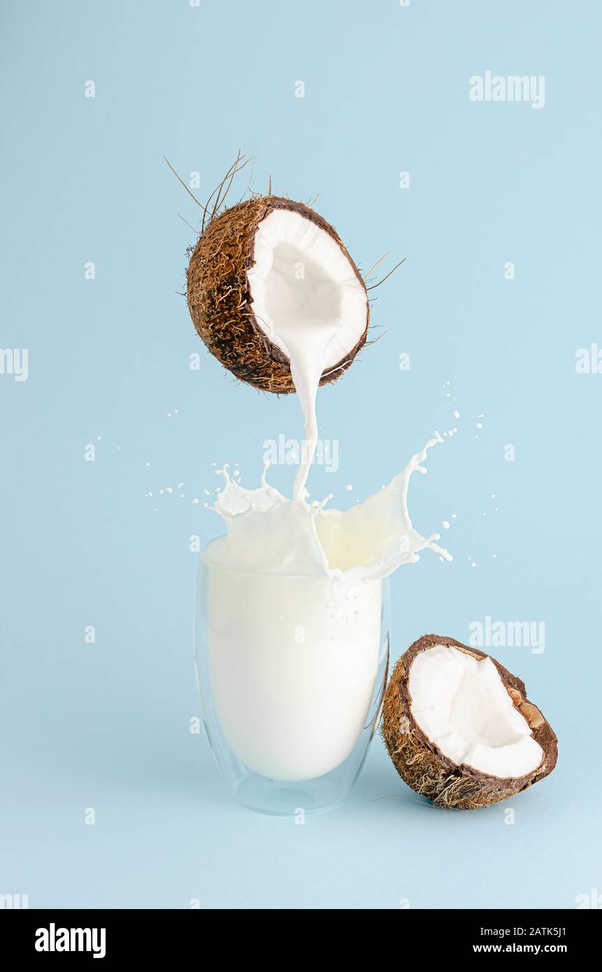 Pouring milk from a coconut and splash in a glass on pastel blue background. Food levitation concept. Vertical Stock Photo