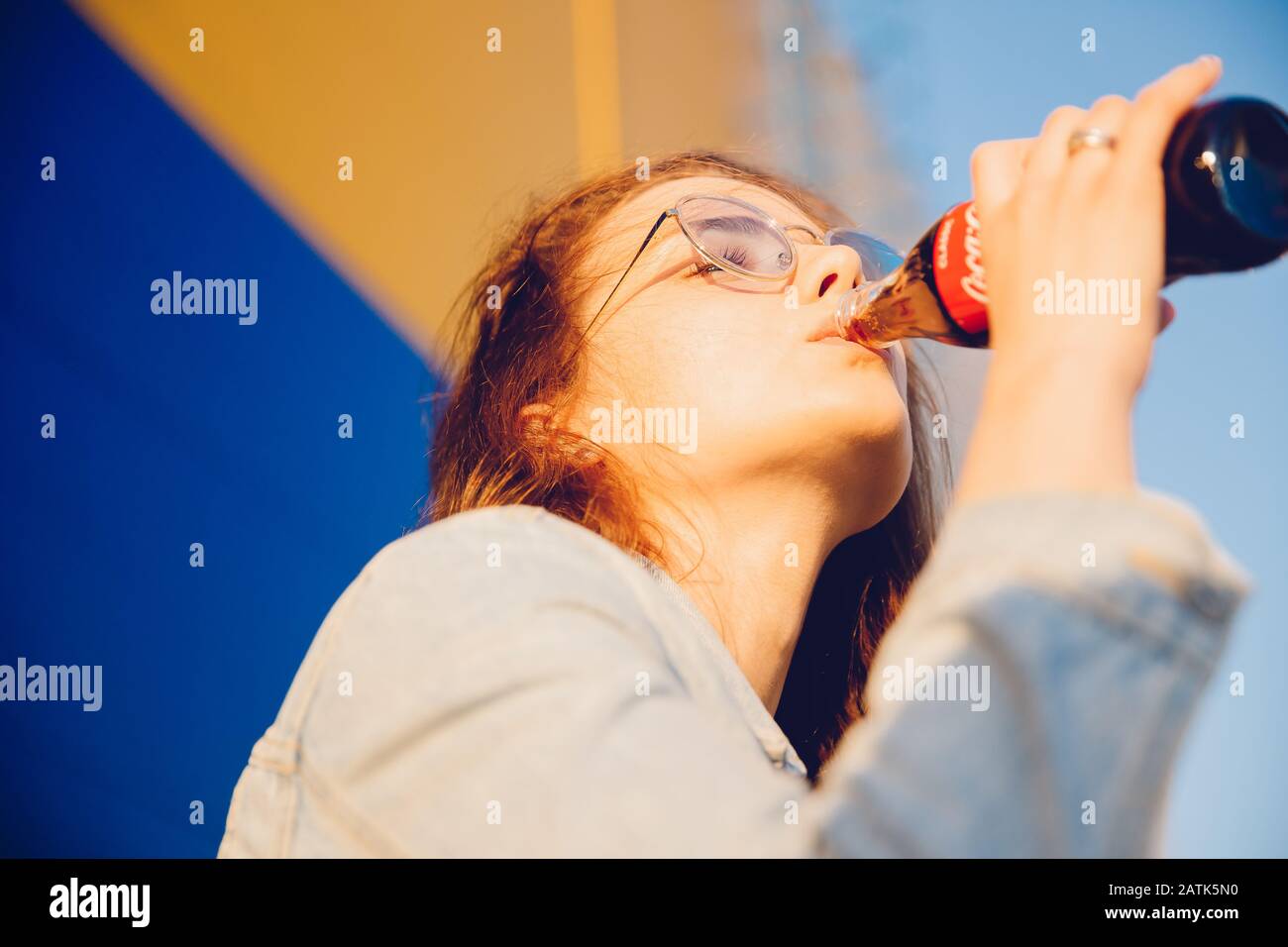 Moscow, Russia - June 27, 2019: Beautiful young woman happy drinking Coca Cola glass bottle soda in hand, sunset Stock Photo