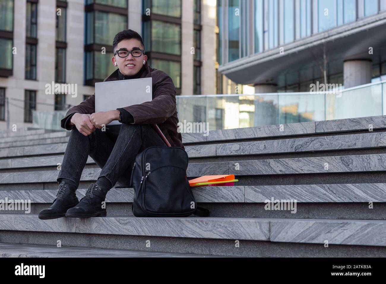 young successful Asian student programmer sit on the steps of the ...
