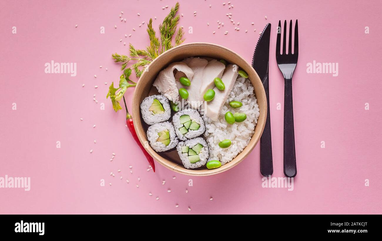 Food banner. Rolls with cucumber, boiled rice, pork, green beans. Asian cuisine fast food delivery. Cardboard bowl, disposable fork and knife on a pin Stock Photo