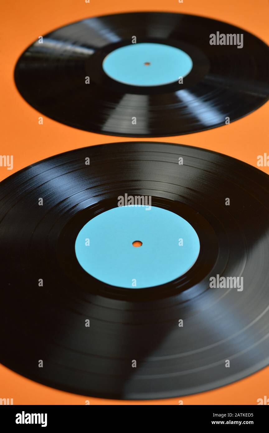 two old black vinyl records with blank cyan labels on orange background Stock Photo