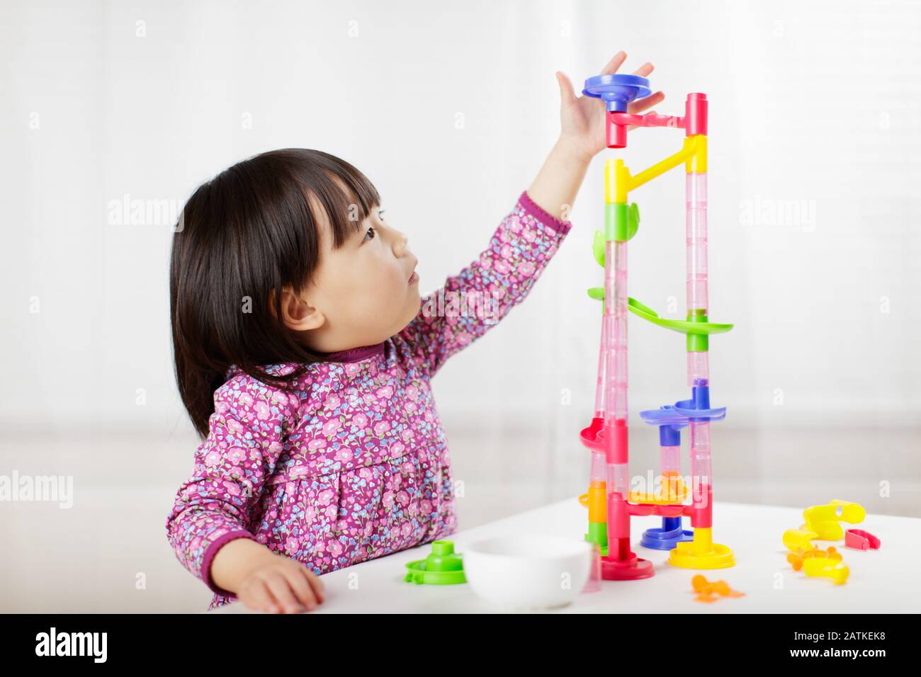 toddler girl play marble run game at gome agianst white background