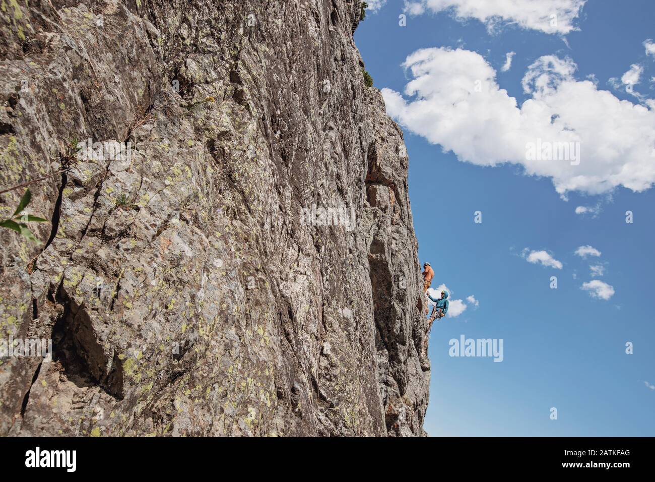 Two people cling to the side of a cliff while rock climbing, Wyoming Stock Photo