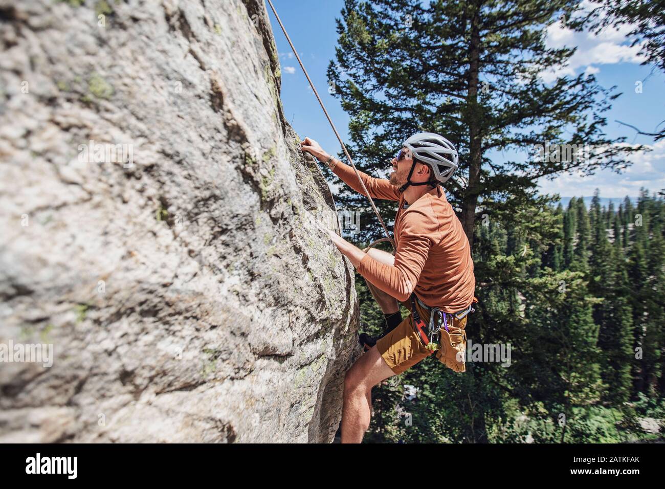 Man holds on to rock with fingertips while climbing with a rope Stock Photo