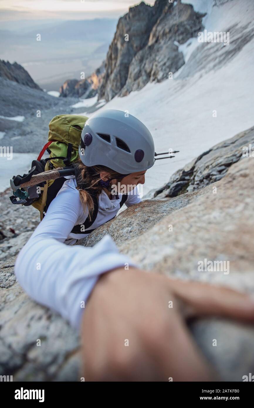 Female rock climber with helmet reaches for a hold on side of cliff Stock Photo
