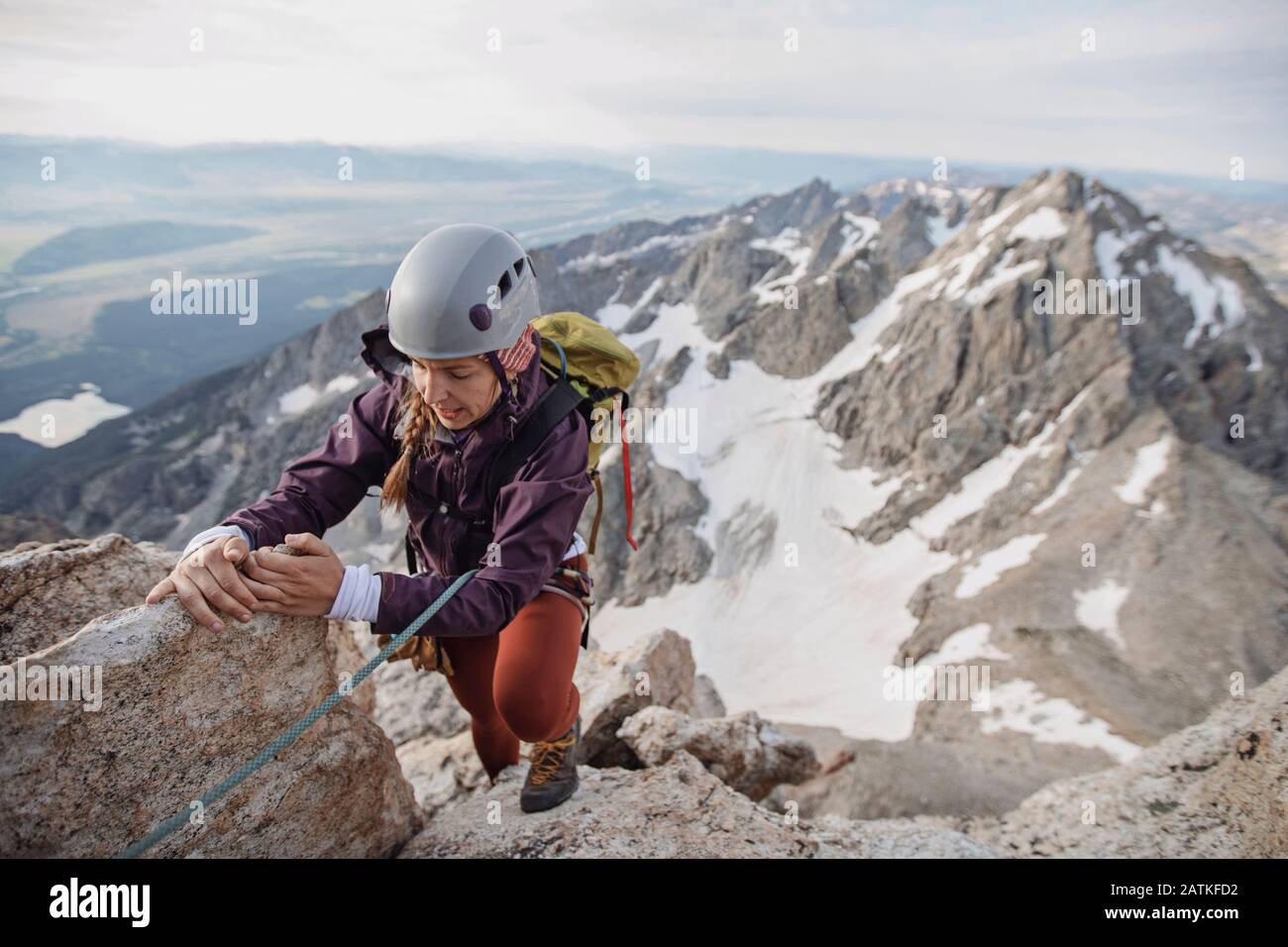 Female rock climber wearing helmet climbs a cliff in the Tetons Stock Photo