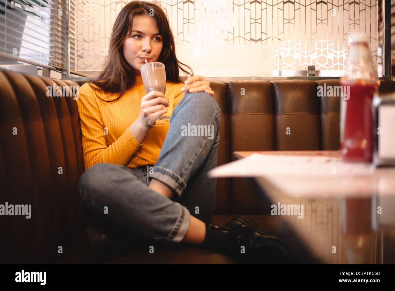 Thoughtful teenage girl drinking chocolate milkshake in restaurant Stock Photo