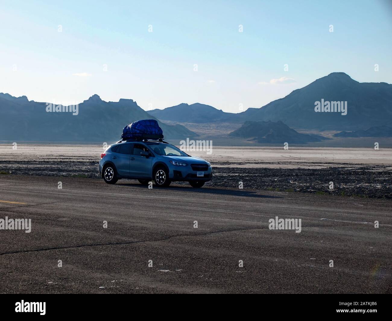 A hatchback four wheel drive automobile packed with camping gear on top is parked on the asphalt next to the Bonneville Salt Flats in the mountainous Stock Photo