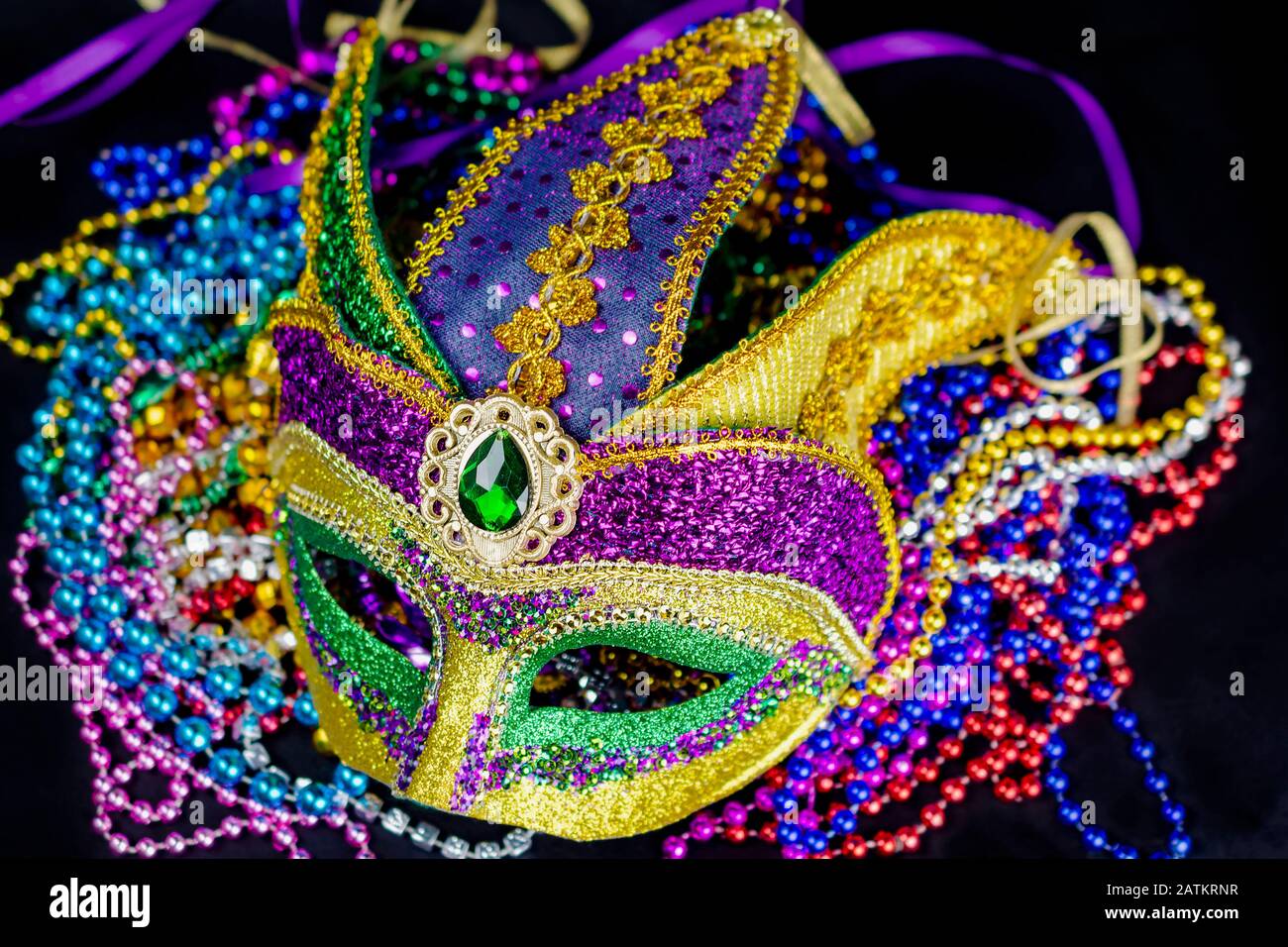 Top down view of a colorful jester mask on a bed of beads. Black ...