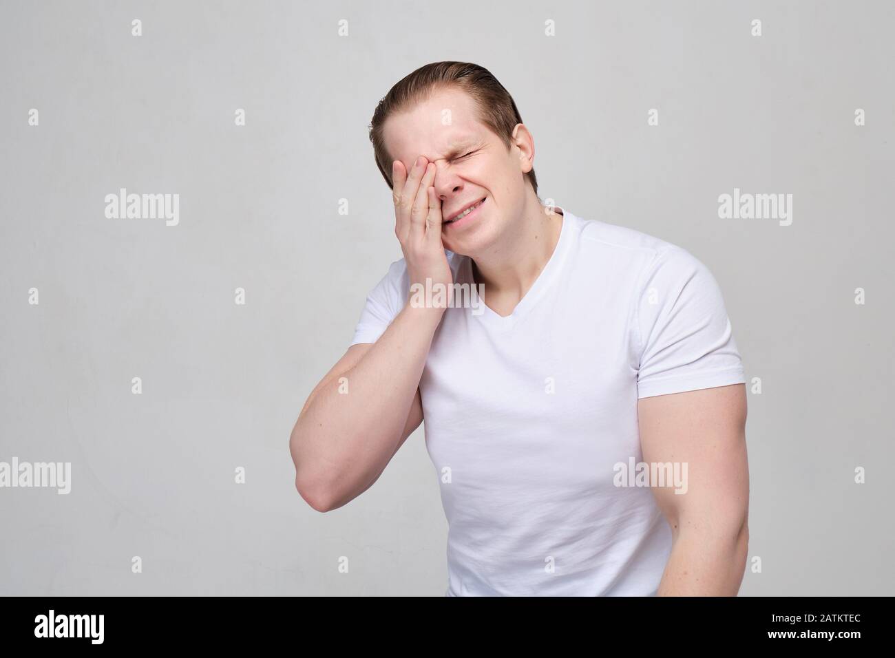 A man with a white T-shirt rubs his eyes in pain. Human vision problems. close up. Stock Photo