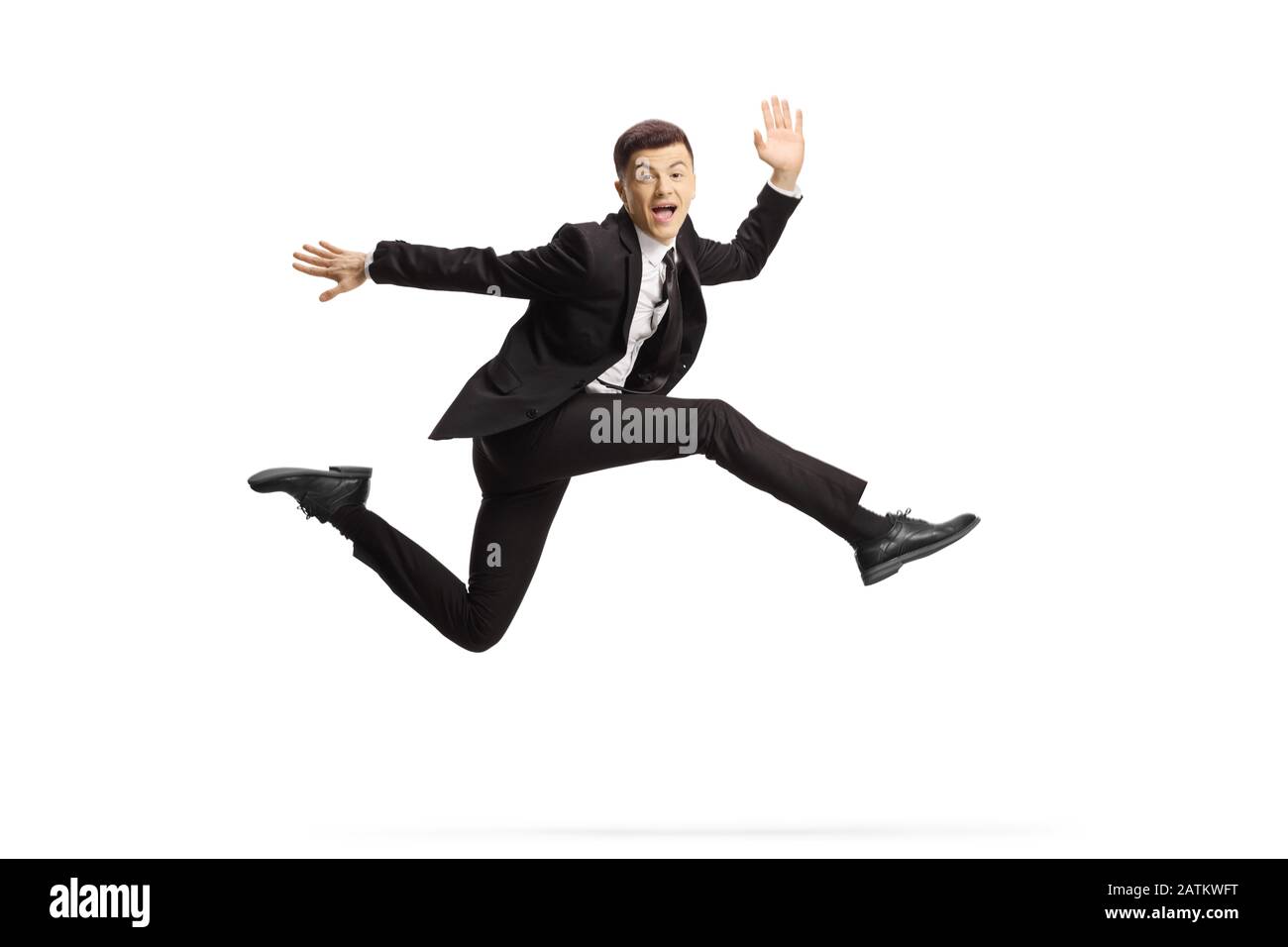 Cheerful young man in a black suit jumping and looking at camera ...