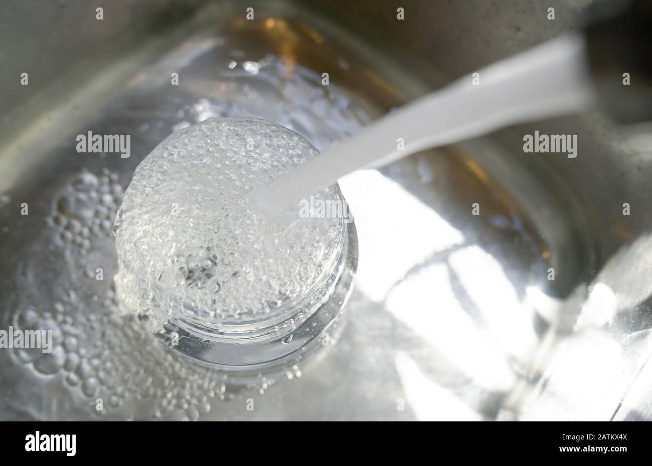 Water from tap into plastic container and it overflow to the sink. Save water concept. Stock Photo