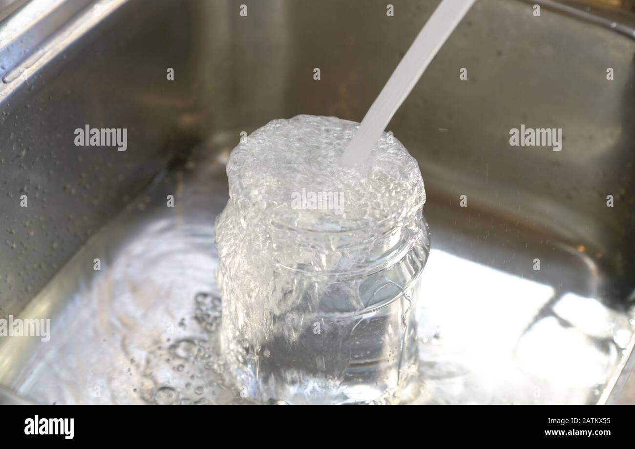 Water from tap into plastic container and it overflow to the sink. Save water concept. Stock Photo