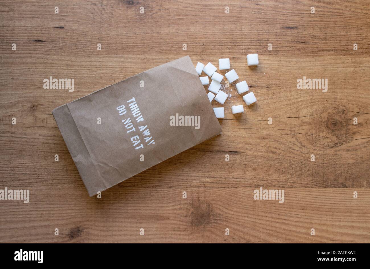 Sugar cubes in the paper pack on the table. 'Throw away, do not eat' excessive sugar intake health warning on the packet. Stock Photo