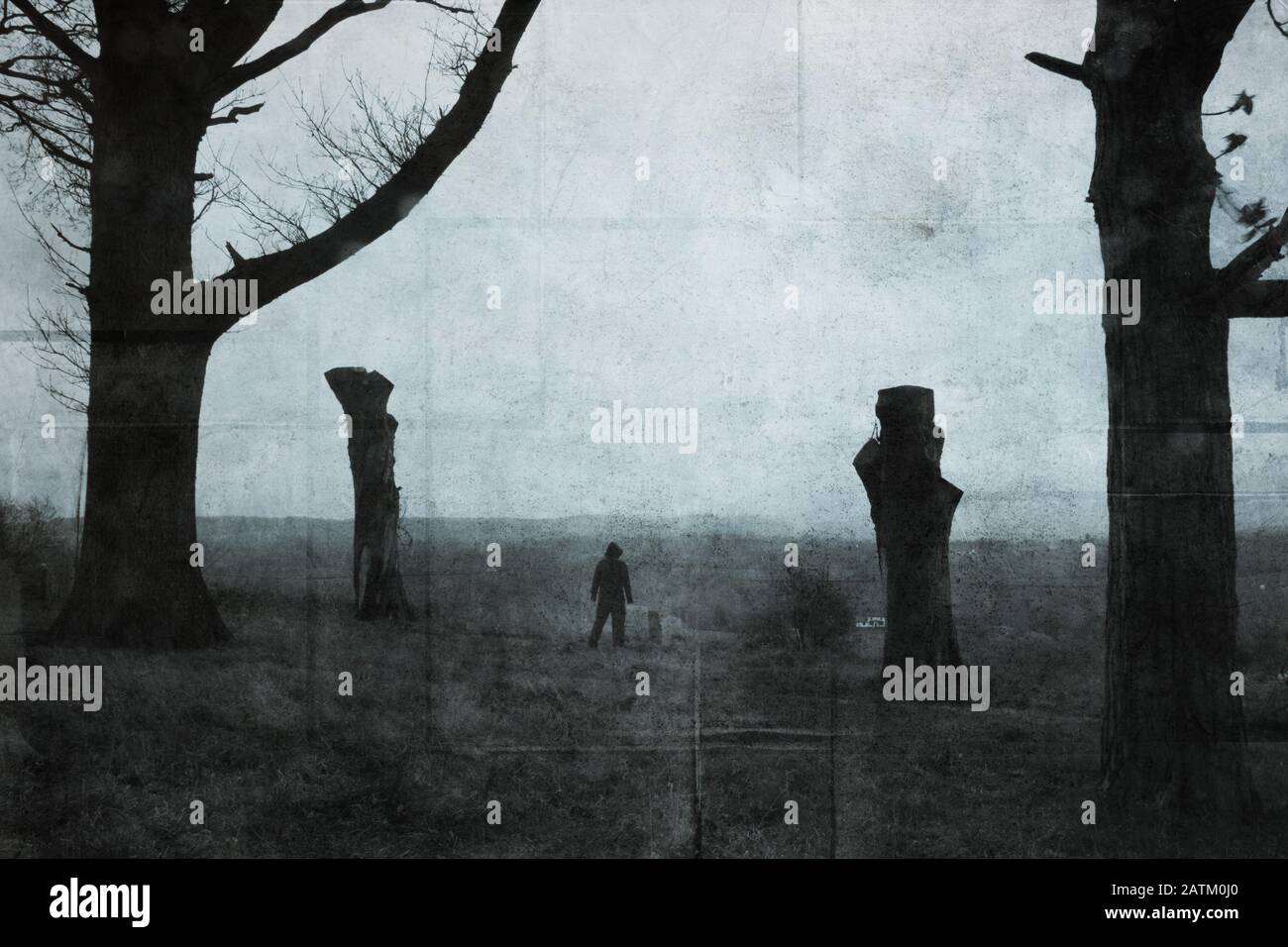 A scary dark hooded figure standing between two trees in the countryside.  With a digital paint effect. With a grunge, textured edit Stock Photo -  Alamy