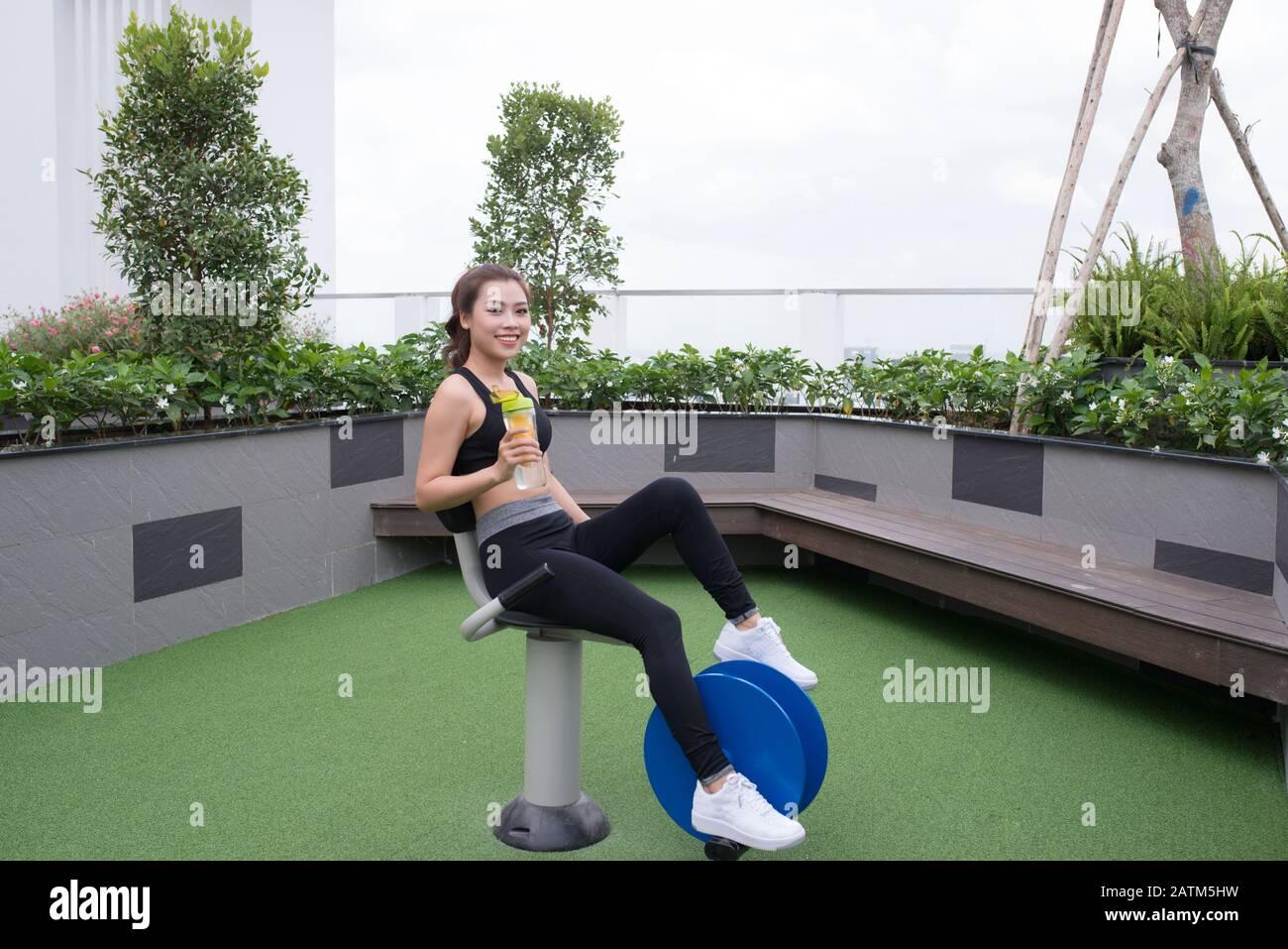 Young asian woman is training on the outdoor playground and drinking water from bottle. Fitness workout gym outdoor Stock Photo