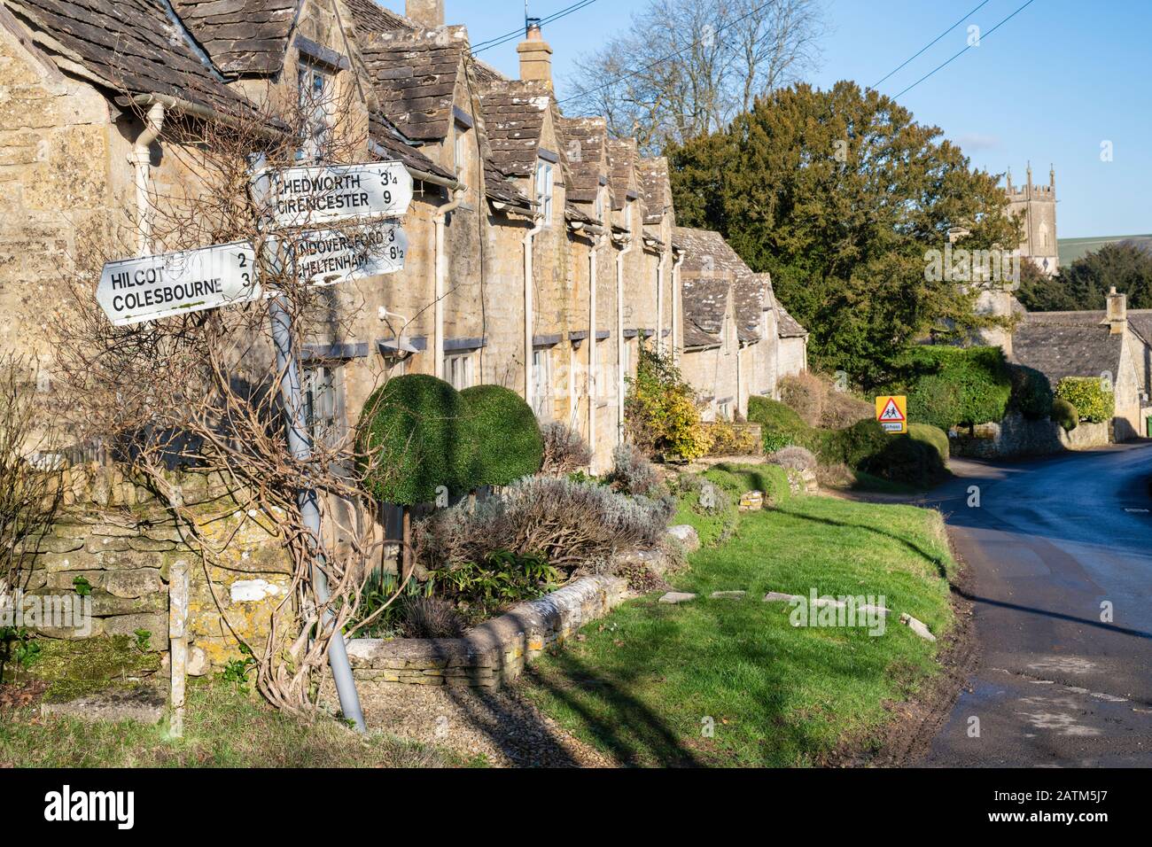 Signpost and Cotswold stone cottages in winter sunlight. Withington, Gloucestershire, England Stock Photo