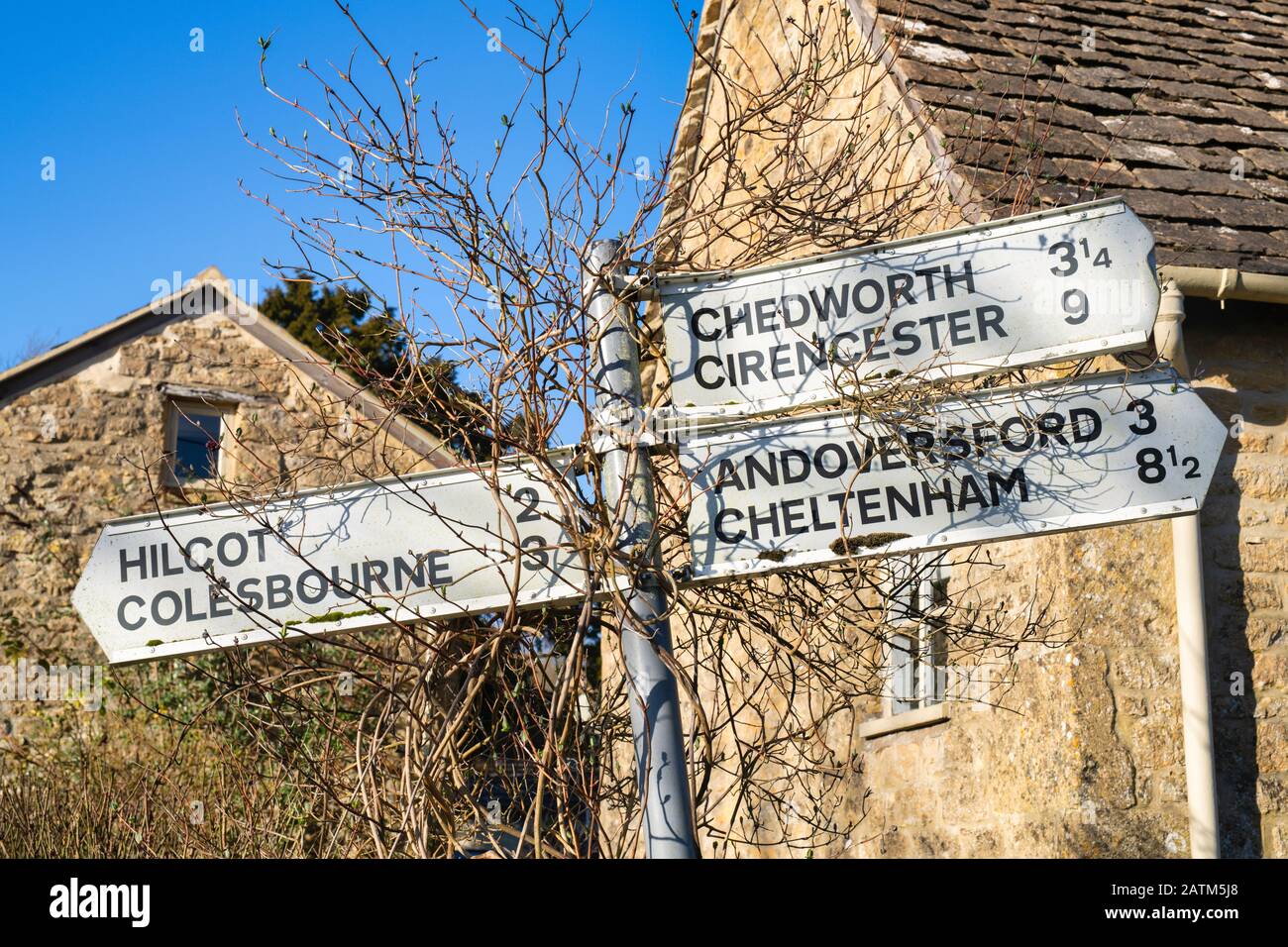 Cotswold village signpost outside a Cotswold stone cottage in winter sunlight. Withington, Gloucestershire, England Stock Photo