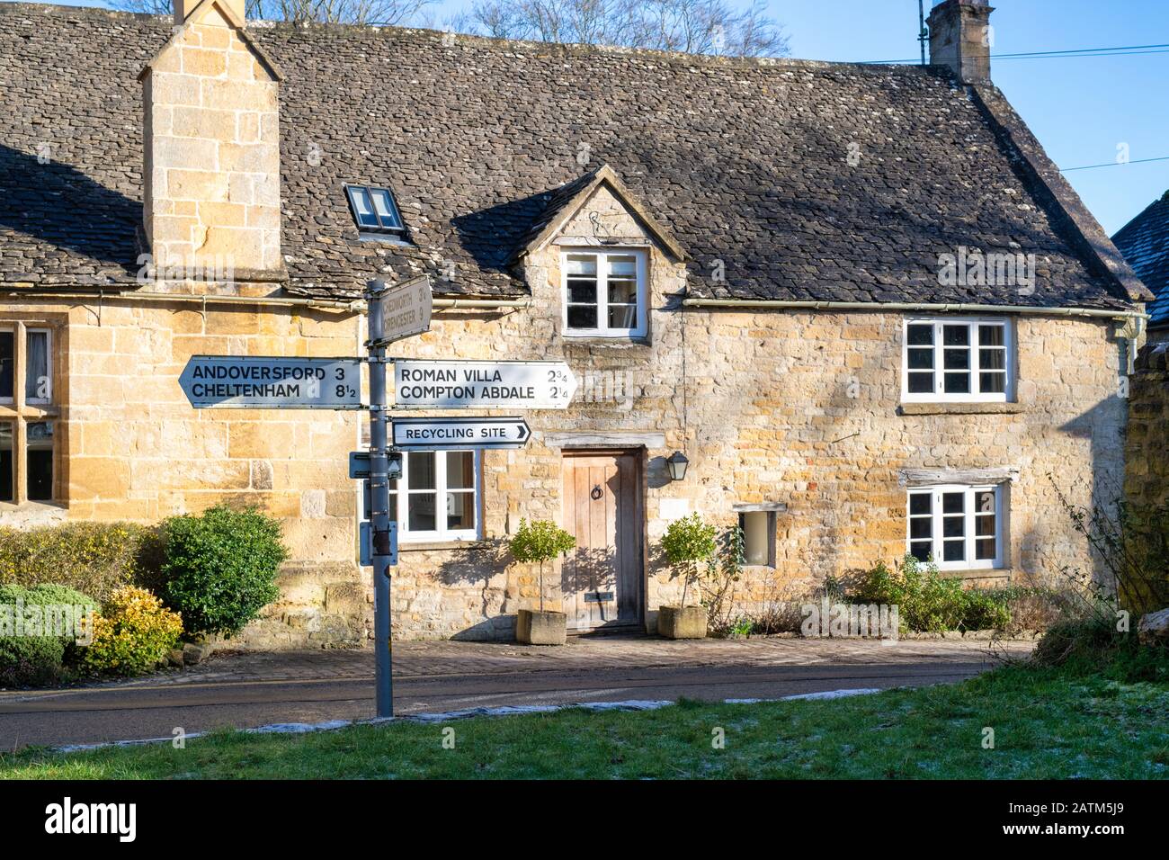 Signpost and Cotswold stone cottage in winter sunlight. Withington, Gloucestershire, England Stock Photo