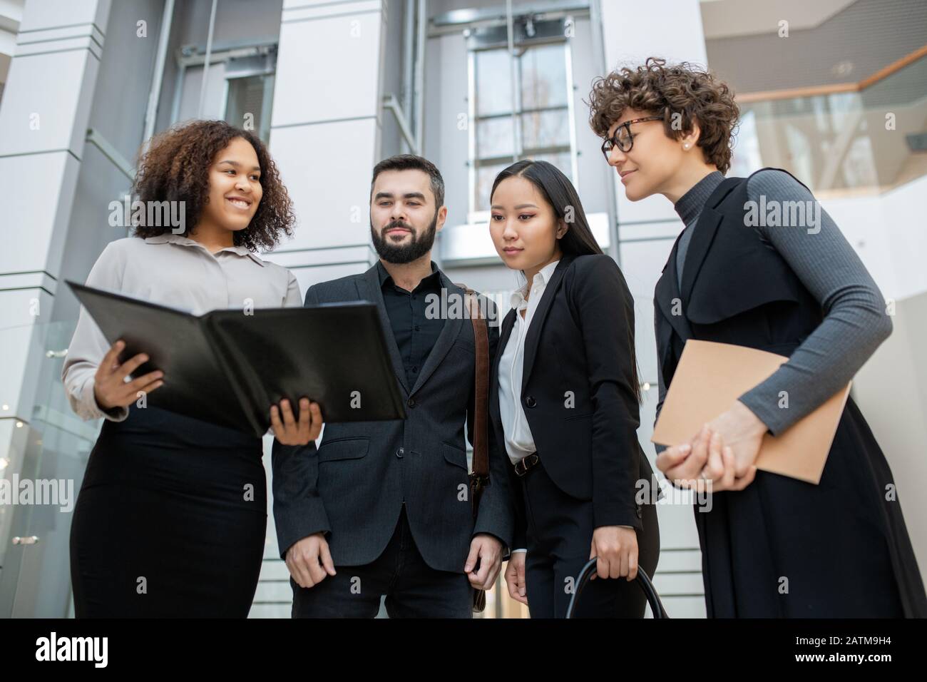 Smiling Afro-American manager holding open folder while presenting project plan to colleagues Stock Photo
