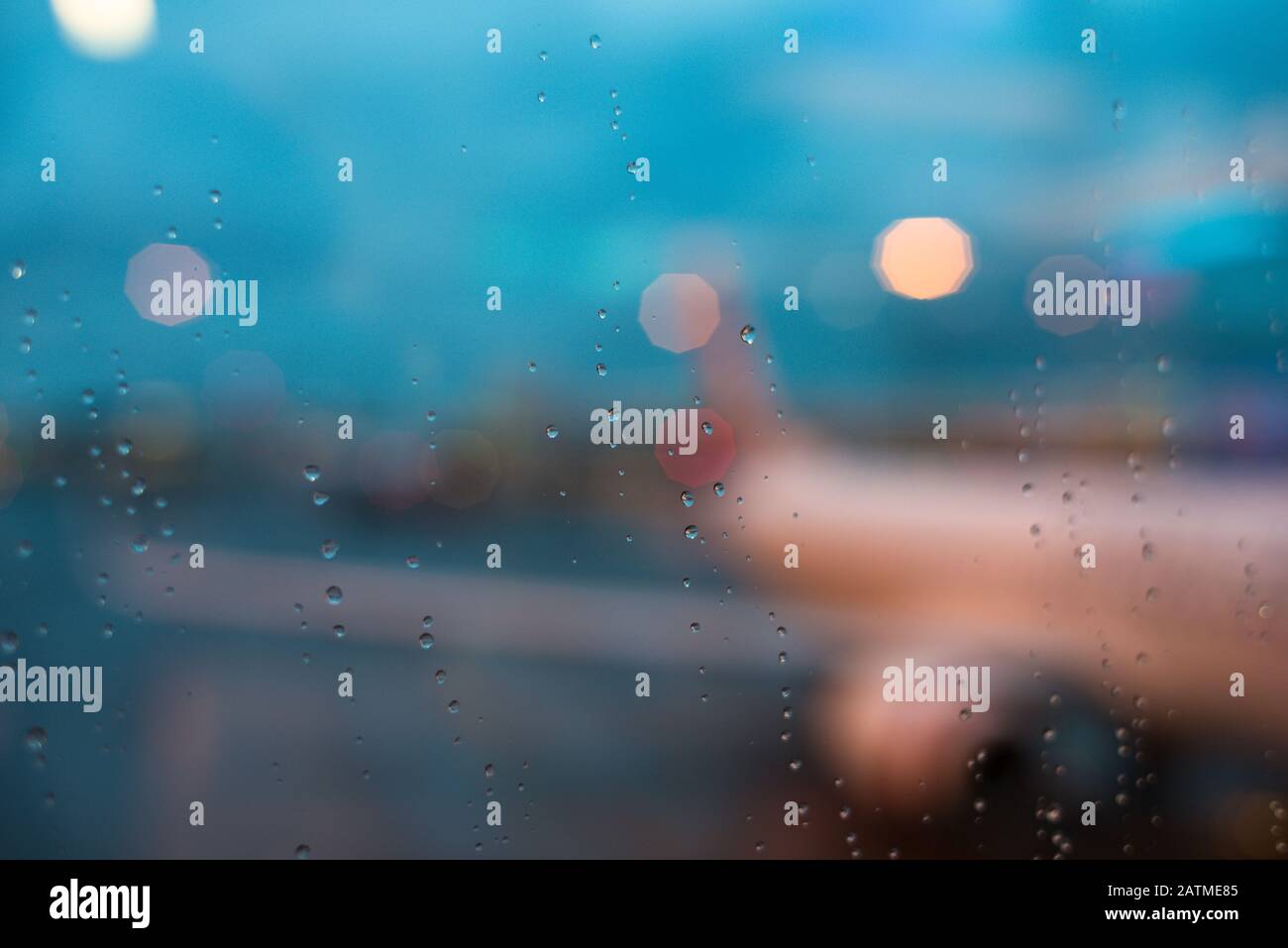 Wet window with water droplets and silhouette of airplane with bokeh lights on the background. Travel delay, rainy weather air travel background Stock Photo