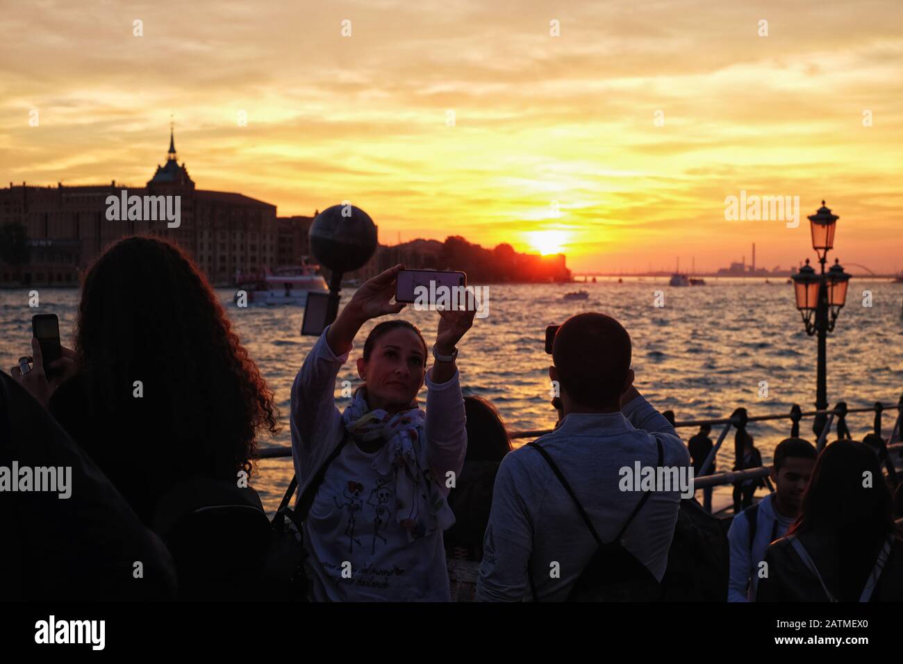 A tourist takes a sunset selfie in Venice Italy, from Dorsoduro at dusk across Giudecca canal, golden light in the sky and on the water Stock Photo