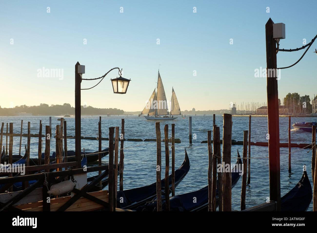 Venice, Italy, a two mast sailboat sails across St Mark's Basin as gondolas float on blue water moored at St Marks early morning by the water. Stock Photo