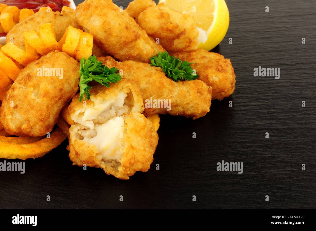 Battered cod nuggets with curly fries on a slate stone background Stock