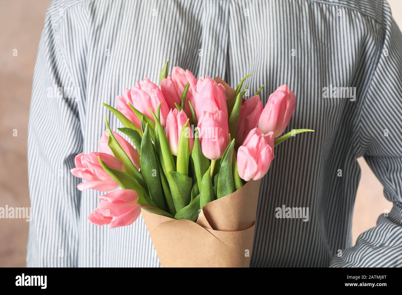 Man holding bouquet of tulips behind his back on brown background, close up Stock Photo