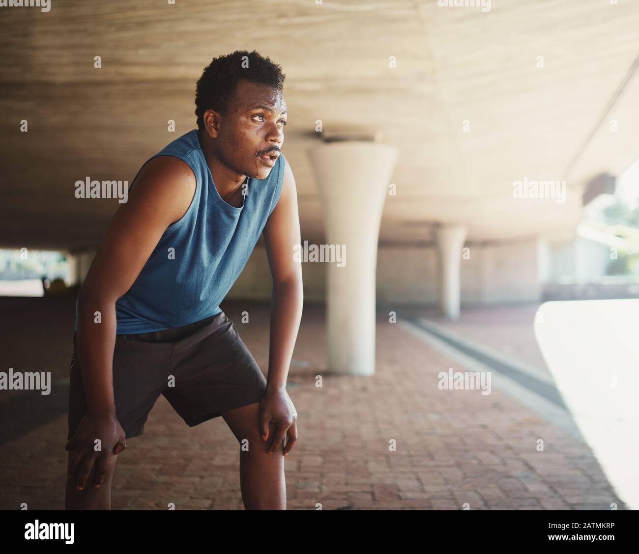 An african american male runner grasping breathe after running on street under the bridge in morning Stock Photo